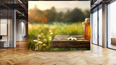 A jar of honey sits on a wooden table in front of a blurred natural background of a green meadow filled with grass flowers and trees creating a backdrop for food drink and product presentations with Wall mural