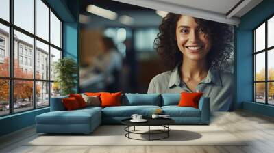 A smiling woman in casual attire holding a pencil and notebook standing in a contemporary office looks at the camera with empty space around her Wall mural