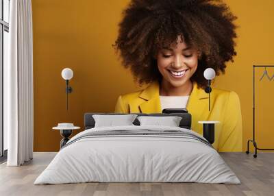 Black woman smiling using phone with yellow background Wall mural