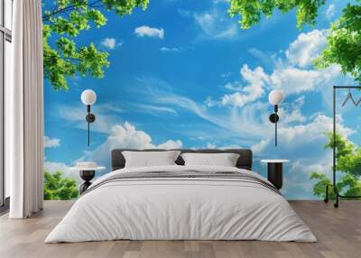 Blank blue sky with fluffy clouds and green tree branches in the foreground providing copy space image Wall mural