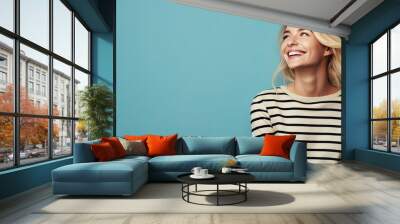 Copy space available for a charming blonde woman in a striped sweater smiling on a blue background Wall mural