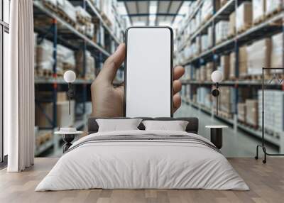 Hand holding a blank mobile phone in a blurred warehouse setting depicting online shopping mobile payments ordering products and business logistics with copy space image Wall mural