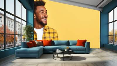 Happy African American man in checkered shirt standing alone looking away in front of yellow background Wall mural