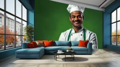 Indian male chef with a warm smile isolated on green background Wall mural