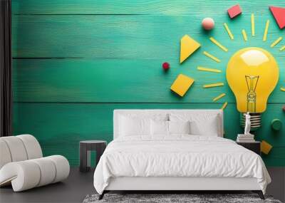 Light bulb radiating rays from vibrant geometric shapes on a green wooden background with copy space. Concept of idea, innovation, and solution, flat lay. Wall mural