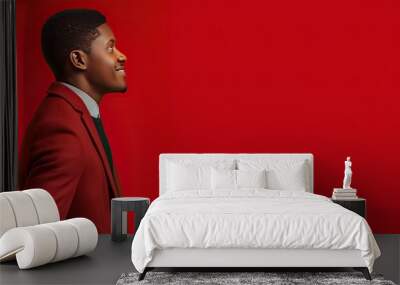 Portrait of a young confident African American businessman in a stylish suit standing with crossed hands and a smile against a vibrant red background Wall mural