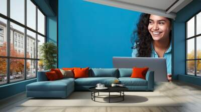 Smiling Indian teen girl using laptop for online study on blue background Happy student in educational webinar Wall mural