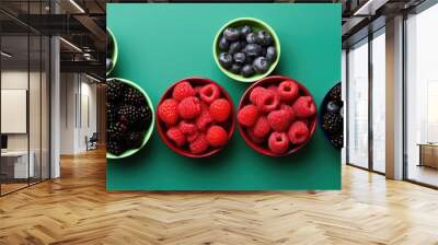 Top view of a vibrant assortment of fresh berries in bowls on a green background with copy space image, conveying a sense of juiciness, freshness, and healthiness. Wall mural