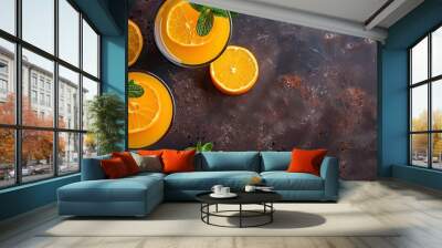 Top view of two glasses of freshly squeezed orange juice garnished with mint, on a dark brown surface with copy space image. Wall mural