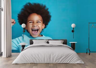 Victorious black boy celebrating with joy standing in blue studio Wall mural