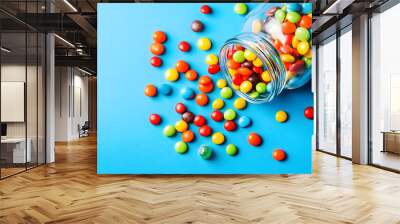 Colorful candy jar overflowing with vibrant sweets on a blue background for National Candy Month celebration Wall mural