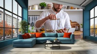 A close-up of a man weighing ingredients on a smart kitchen scale, ensuring precise measurements for his recipe. This high-tech gadget aids in accurate cooking for perfect results. Wall mural