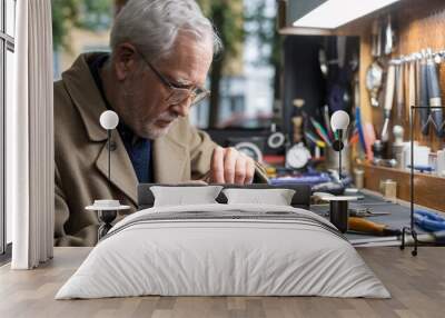 Elderly Craftsman Repairing Watches in Workshop. An elderly man with white hair and glasses is meticulously repairing watches at a well-organized workbench.  Wall mural