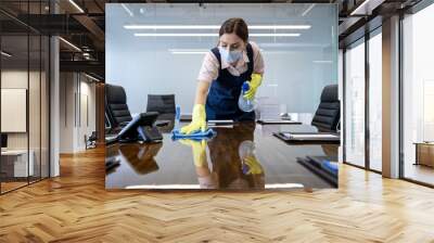 Office Cleaning Staff Sanitizing Conference Table. A dedicated cleaning professional in a blue uniform and yellow gloves meticulously cleans a glass table in a contemporary office setting.  Wall mural