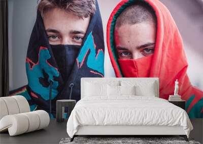 Two young individuals stand side by side, their faces partially obscured by vibrant, colorful hoodies and masks, exuding an air of mystery and confidence. Wall mural