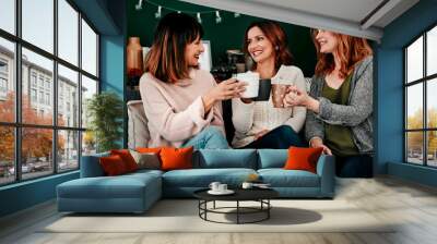 Cheers, friends and women on couch with smile for celebration, holidays and reunion in home. Coffee, happiness and together in living room for vacation, connection and toast with tea in apartment Wall mural