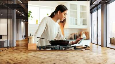 Woman, cooking and phone by stove in kitchen for healthy online recipe, meal prep or ingredients research. Nutrition influencer, food blogger or vegan chef with tech for social media tutorial in home Wall mural