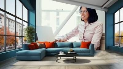 Working through my day with a smile. Cropped shot of an attractive young businesswoman sitting alone and using her laptop in the office. Wall mural