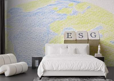 There is a cube stamped with the letters of the ESG on top of a sketchbook with a picture of the earth. Wall mural