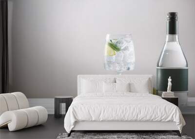 cold glass of gin tonic and bottle on white wooden base on light background Wall mural