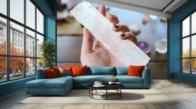 Large Selenite Rod, Holding Crystal over wooden table. Women's hand holding selenite in natural lighting. Healing selenite chunk, large witch wand. Wiccan healing crystal tools, zen meditation stones. Wall mural