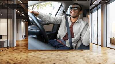 A joyful african american in glasses dances in a car, sings while driving his car. Road fun Wall mural