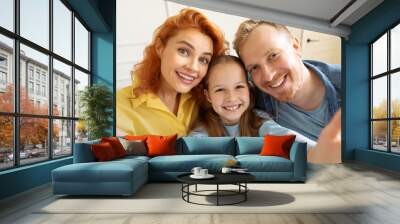 Cheerful family, mom dad and daughter making selfie or recording video at home, smiling at camera Wall mural