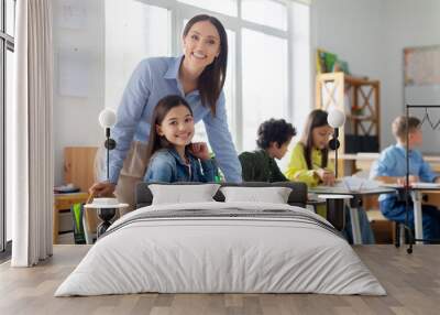 Cheerful young female teacher working in elementary school, happy teacher and girl smiling at camera in classroom interior Wall mural