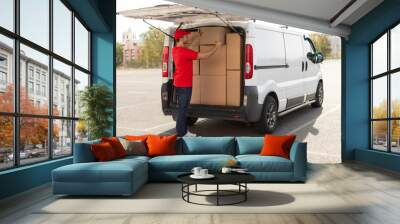 Courier man loading cardboard boxes to van, preparing for delivering postal parcel, outdoors shot Wall mural