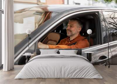 Handsome European middle aged man driving brand new car, looking at road and smiling, enjoying his new automobile Wall mural