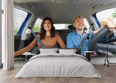 Happy European spouses going on trip by car, man and woman sitting in their comfortable auto, looking at road and cheerfully smiling Wall mural