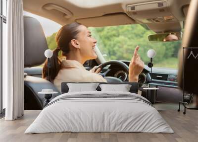 Happy excited young woman driver sitting in front seat, holding auto steering wheel and enjoy listening to music, have fun, copy space Wall mural