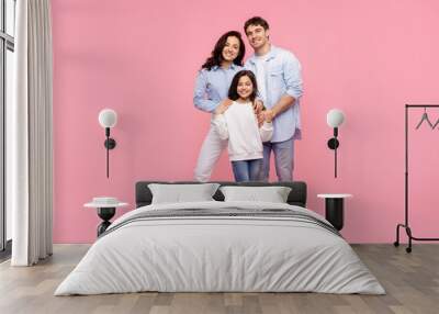 Happy mom dad with child daughter cuddling and smiling at camera, posing isolated on pastel pink background, full length shot Wall mural