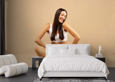 Healthy fit body. Young excited lady sitting in white underwear isolated on beige studio background and smiling Wall mural