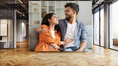 Indian lovers couple enjoying time together at home, happy man and woman embracing and talking, sitting on couch in living room Wall mural