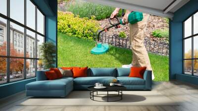 Man cutting fresh green grass with an electric trimmer on his garden lawn, taking care and doing seasonal garden works Wall mural