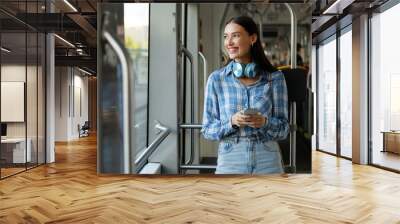 Passenger woman in tram indoor, standing enjoying her journey through the city inside modern streetcar, looking aside and smiling. Commute and connectivity Wall mural