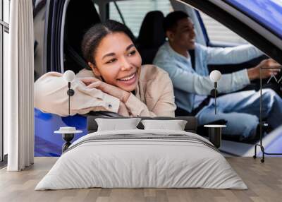 Smiling african american couple driving car enjoying first ride together, woman sitting in front passenger's seat looking through opened window Wall mural