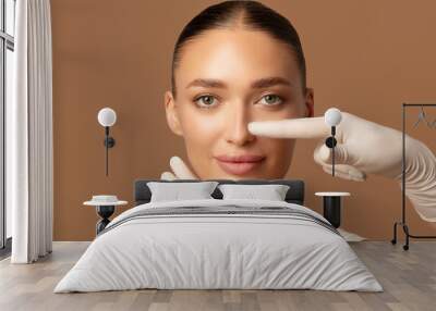 Surgeon hands touching woman nose, examining lady before plastic surgery on brown studio background Wall mural