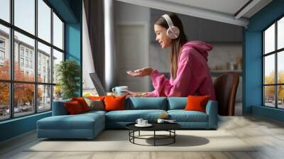 Teen schoolgirl in headphones studying online with remote tutor from home, student using laptop talking in webcam video chat learning lesson with distance teacher Wall mural