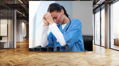 Tired exhausted young female nurse or doctor standing outside hospital, crying and feeling stressed after hard working day Wall mural