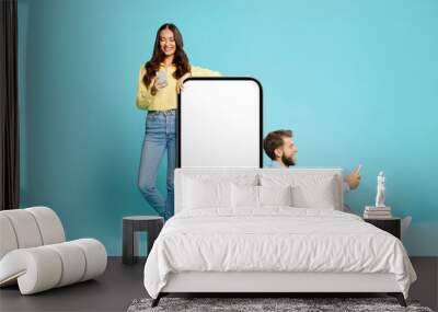 Young European couple near oversized smartphone blank screen, ideal for showcasing apps or websites, man and woman using their cellphones Wall mural