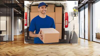 Young smiling delivery man courier with cardboard box in hands outdoors. Delivery and shipping concept Wall mural