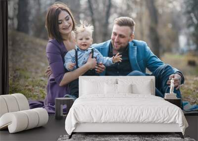 Happy family in the park evening light. The lights of a sun. Mom, dad and baby happy walk at sunset. The concept of a happy family.Parents hold the baby's hands. Wall mural