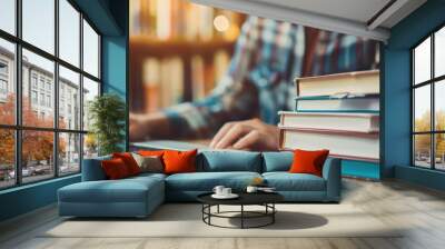 A person is typing on a laptop in front of a stack of books Wall mural