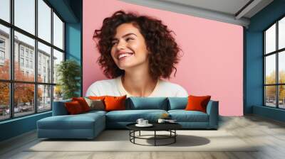 Close up studio shot of beautiful young mixed race woman model with curly dark hair looking aside with charming cute smile while posing against pink blank copy space wall for your content Wall mural