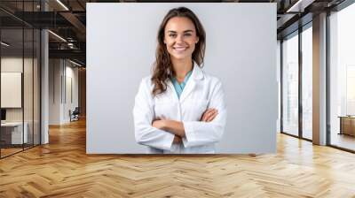 Smiling young woman, graduate student medical therapist or pediatrician, standing in a medical gown with a stethoscope on her shoulders on a white isolated background  Wall mural