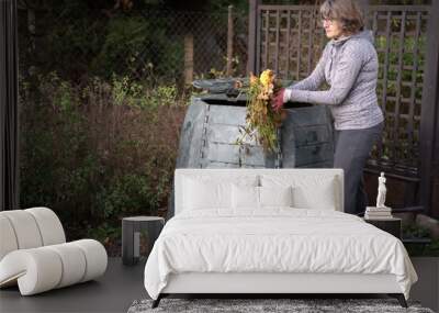 Middle aged caucasian woman throwing garden waste from wheelbarrow into compost bin in garden. Zero waste, sustainability and environmental protection concept Wall mural