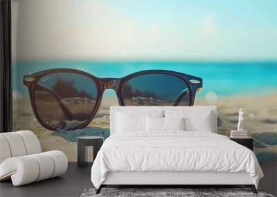 Black sunglasses on sandy beach, ocean background, clear blue sky, summer vacation, close-up, shallow depth of field, soft focus, warm tones, tranquil atmosphere, travel concept. Wall mural