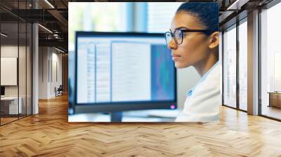 Doctor in a lab coat, glasses; Mixed race;  female looking carefully at a monitor, a woman in medicine examining health data, hospital staff background. medical profession - natural light, daytime Wall mural